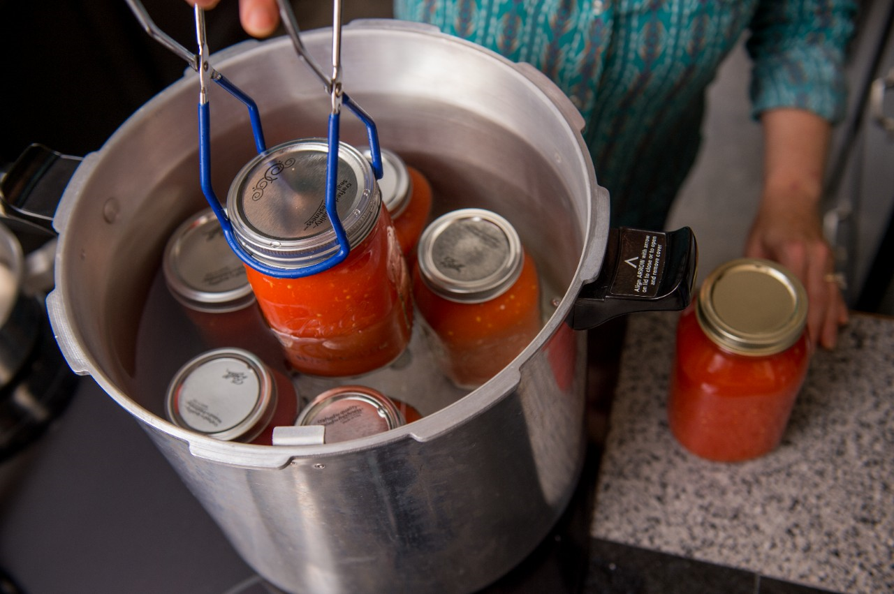 Image of someone pulling canning jars out of a water bath.