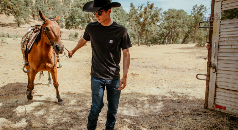 Rancher leads horse into shady barn on extremely hot day