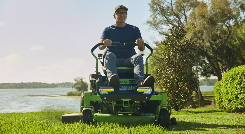 Person using electric zero-turn mower to cut grass near shoreline of lake